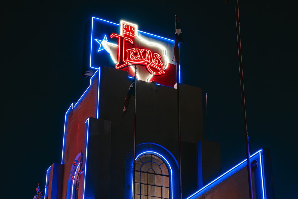 The Billy Bob's Texas neon sign lit up against the night sky above the building's blue neon outline