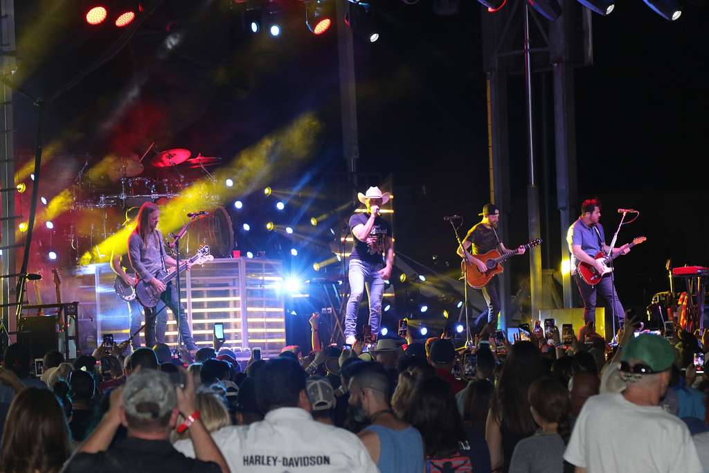 A country band playing a lit stage in cowboy hats while a packed crowd watches